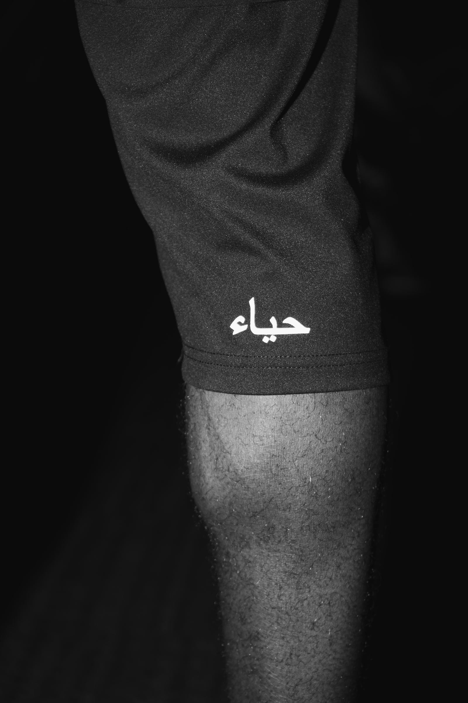 Macro of the legging cuff in black and white, showing the fabric weave, the hem seam and the حياء wordmark