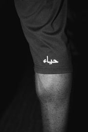 Macro of the legging cuff in black and white, showing the fabric weave, the hem seam and the حياء wordmark